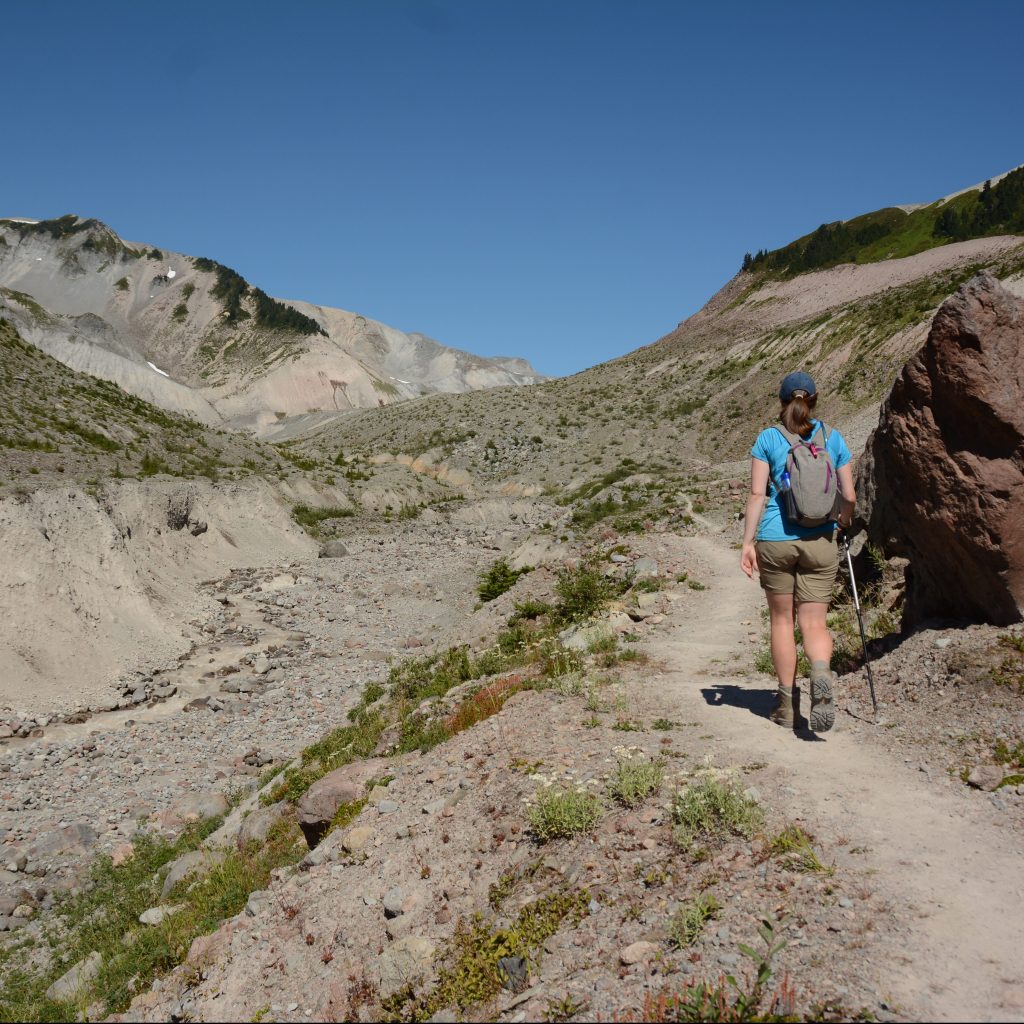 A female hiker is back-on to the camera and hikes up a sandy alpine moraine towards Opal Cone, past Elfin Lakes in Garibaldi Provincial Park in British Columbia, Canada.