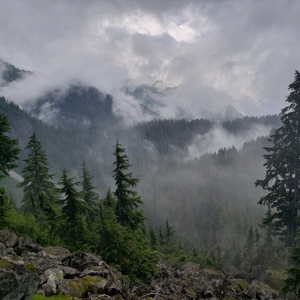 Low clouds and fog hug the mountains and forest on the trail to Elsay Lake near Mount Seymour in Mount Seymour Provincial Park near Vancouver, BC.