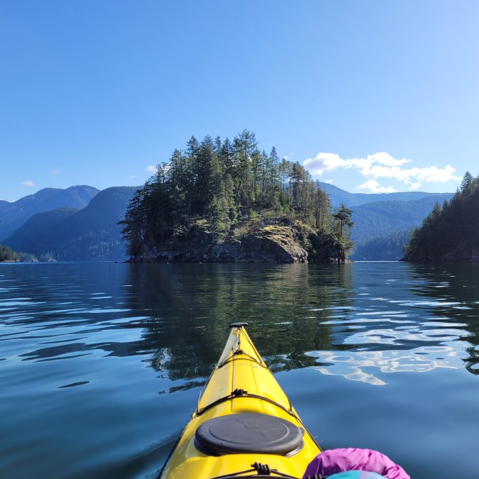 A kayaker paddles towards Jug Island on a sunny day with calm waters in Indian Arm. Jug Island is located near Belcarra Regional Park in Vancouver, BC.