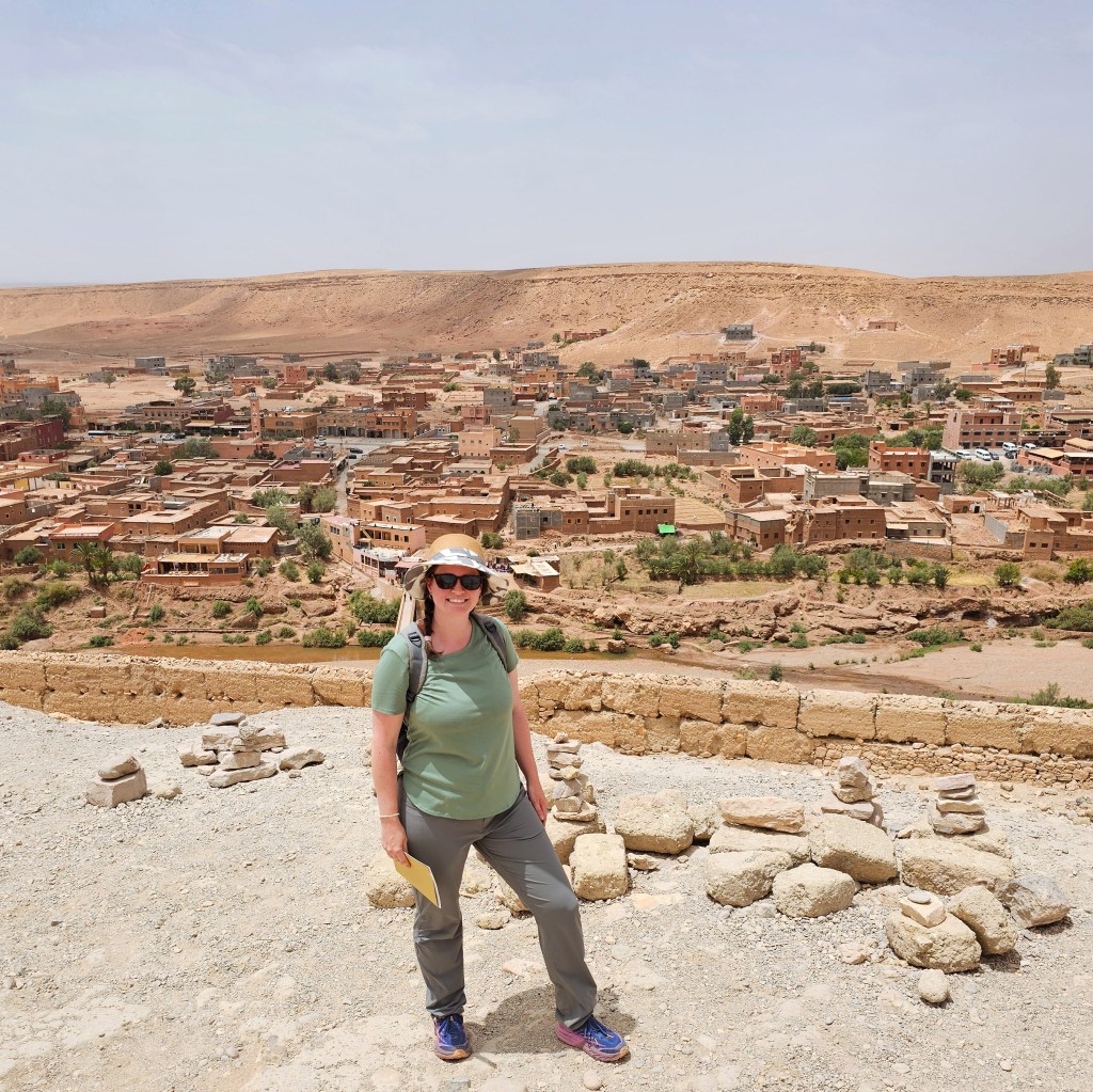 A female traveller smiles at the camera in front of the adobe houses and desert outside Marrakech, Morocco at the UNESCO Work Heritage Site Ait Benhaddou.