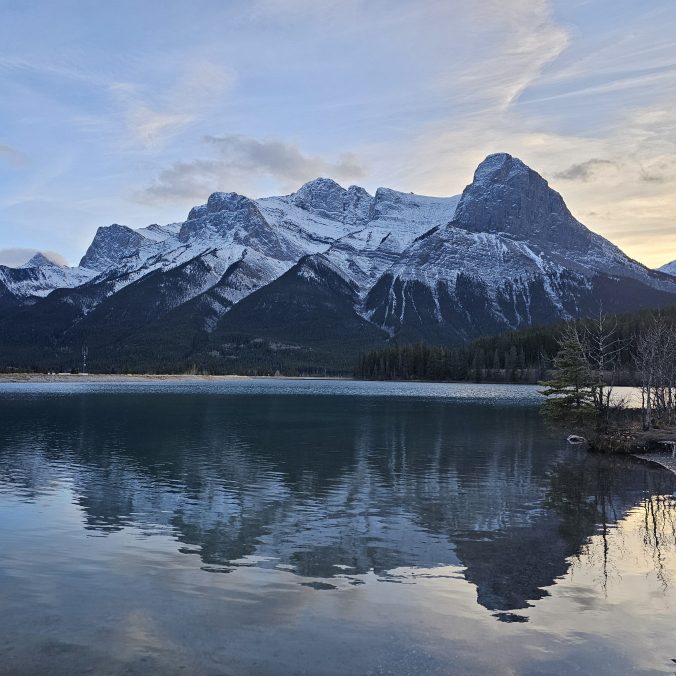 A photo of the mountains with a fresh sprinkle of snow, with a lake in the foreground during sunset in Canmore, Alberta in the Rocky Mountains.