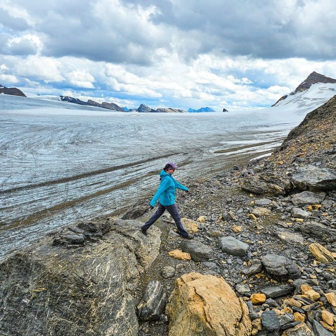A female hiker walks in front of an epic glacier icefield at the top of Snowbird Pass in Mount Robson Provincial Park, off the Berg Lake Trail, in BC.