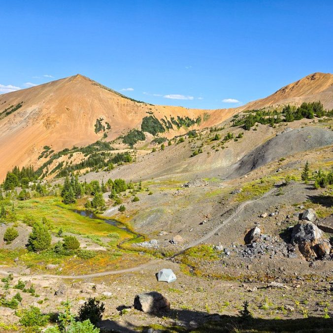 A photo of a tent wild camping in the Taylor Basin Wilderness near South Chilcotin Provincial Park, with Taylor mountain in the background and the barren meadows of the alpine.