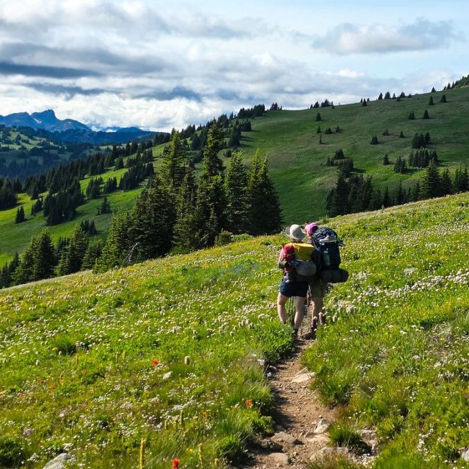 Two female hikers admire the view of the alpine meadows, wildflowers, and mountains on the Heather Trail in Manning Provincial Park, BC.